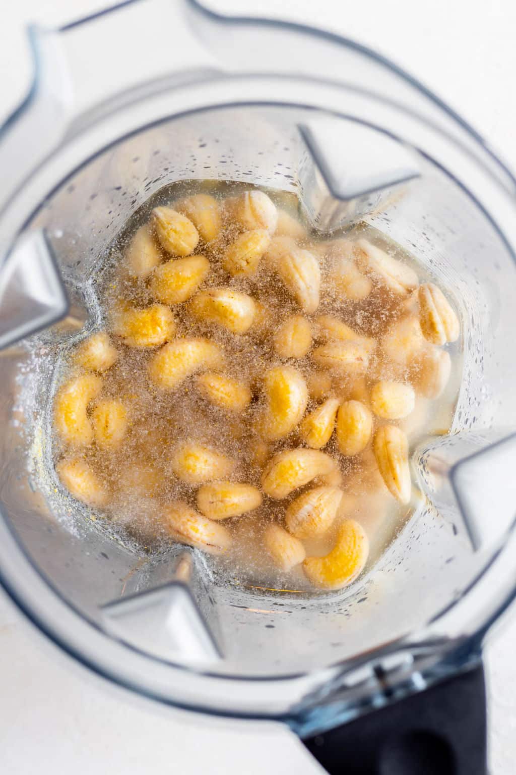 overhead view of cashews and clear liquid in a blender.