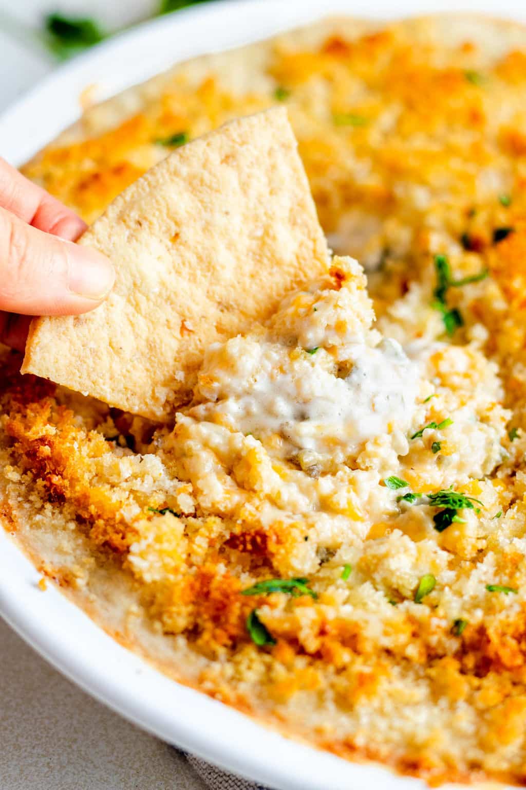 dipping a tortilla chip into a baked white dip.