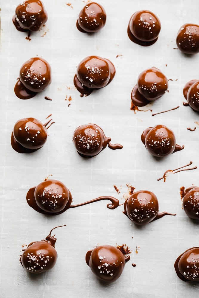 rows of chocolate truffles covered in melted chocolate on a parchment-lined baking sheet.
