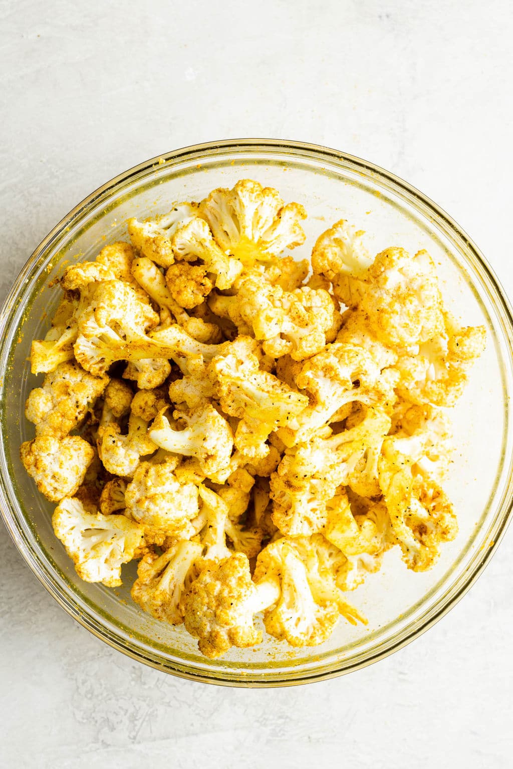 a glass bowl filled with yellow curry-seasoned cauliflower florets.