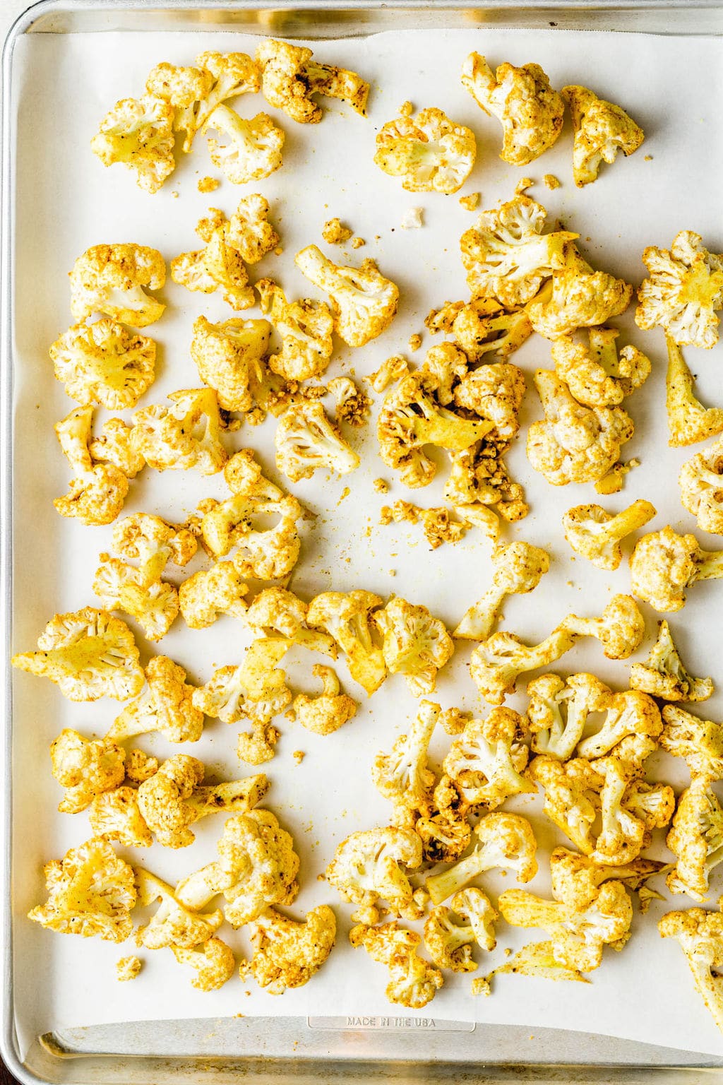 Yellow curry-seasoned cauliflower florets on a parchment lined baking sheet.