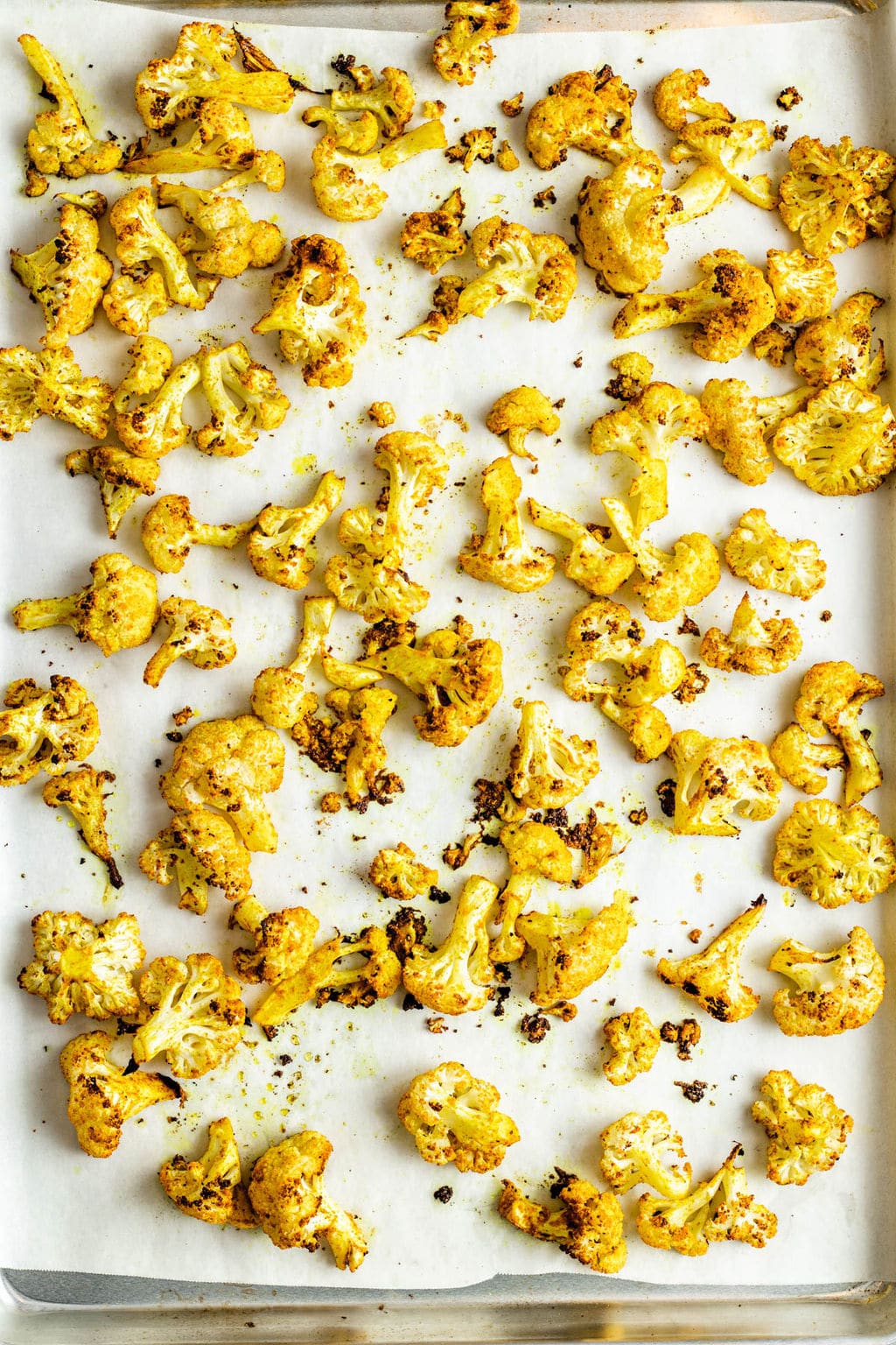 Yellow curry-seasoned roasted cauliflower florets on a parchment lined baking sheet.