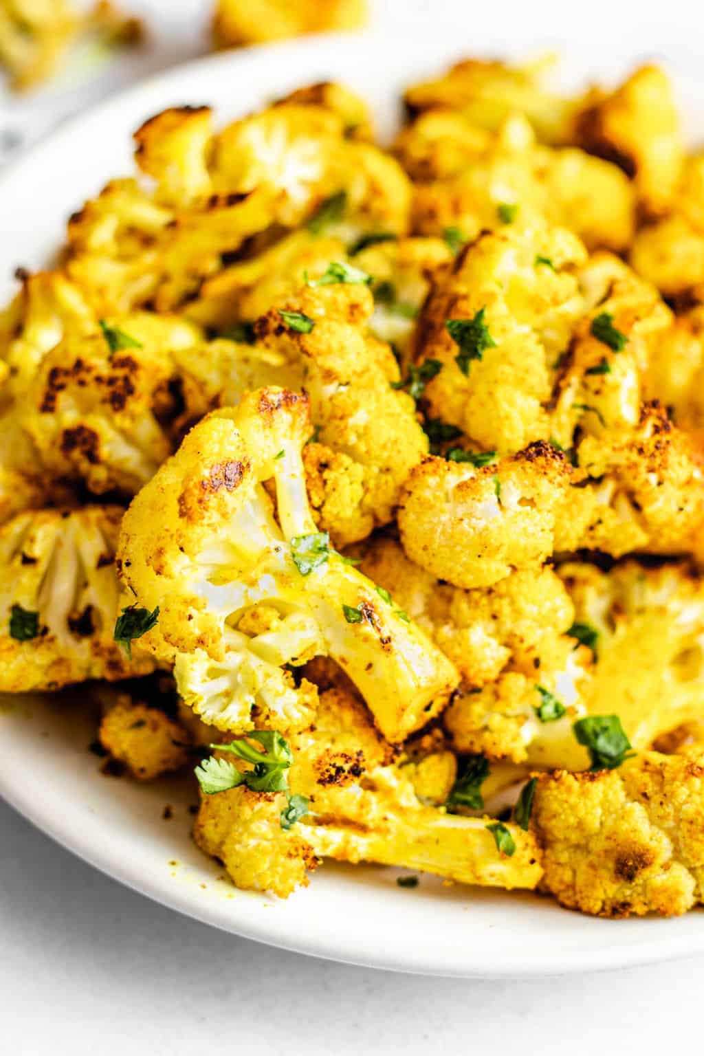 close up on a pile of roasted curried cauliflower on a white plate.