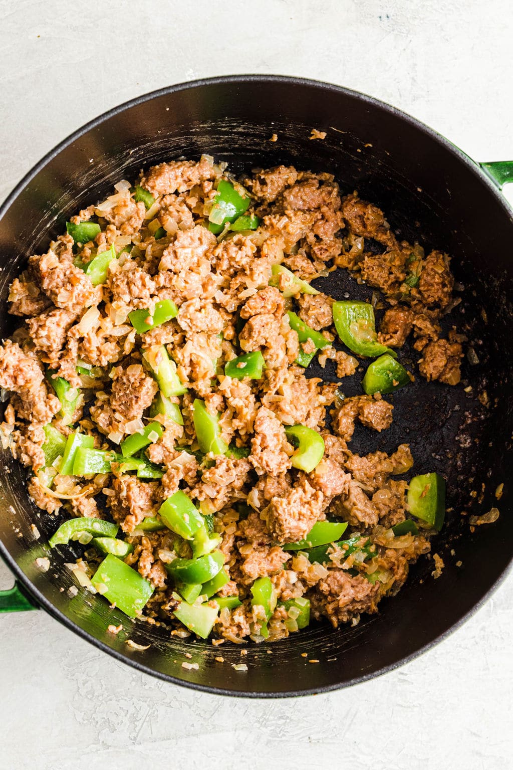 sautéing vegan ground beef and green peppers in a large black pot.