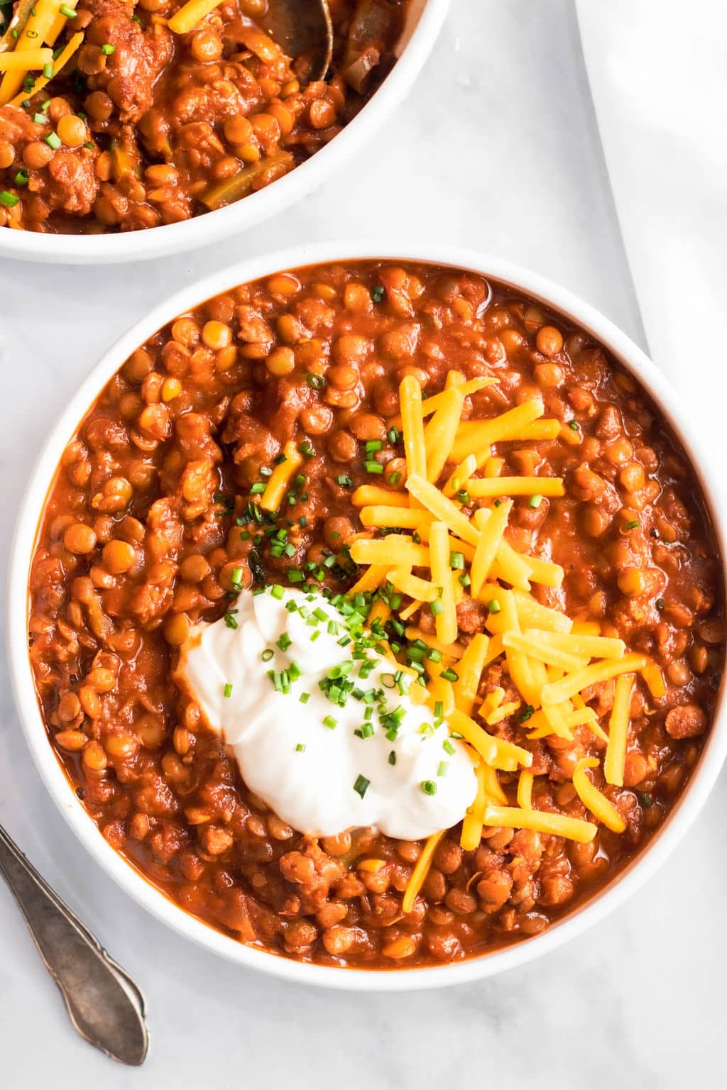 a white bowl filled with lentil chili and topped with shredded cheese and sour cream.