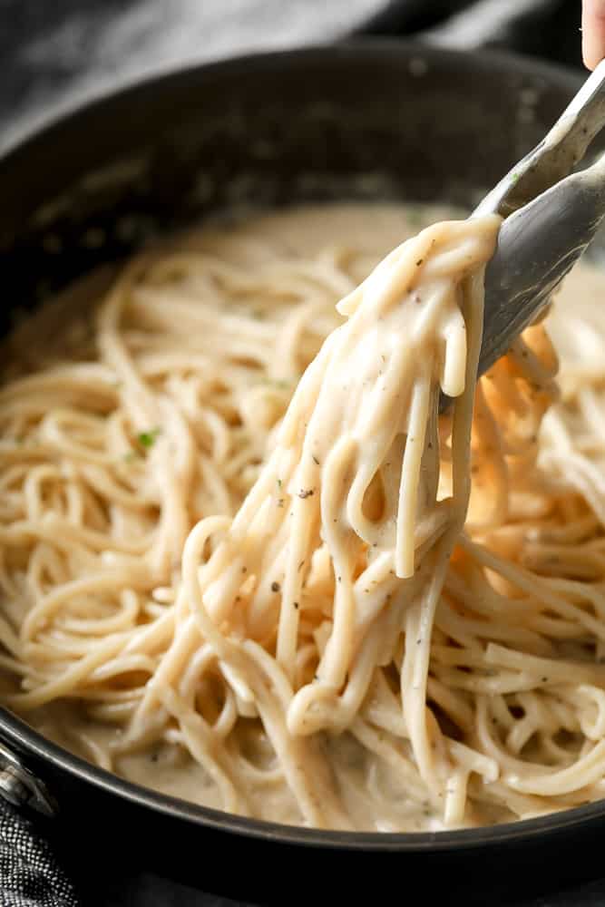 tongs lifting creamy pasta from a pan