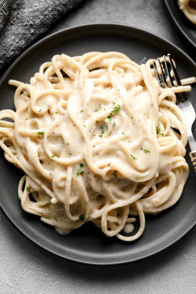 grey plate on black background with a fork and dairy free alfredo sauce mixed with noodles