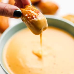 square photo of a pretzel being dipped into vegan beer cheese sauce