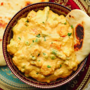 close up of yellow curry in pretty reddish bowl with naan