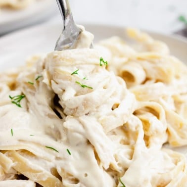 fork holding lots of pasta with white sauce