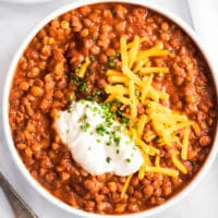 a white bowl filled with lentil chili and topped with shredded cheese and sour cream.