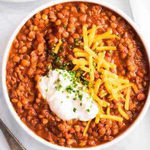 a white bowl filled with lentil chili and topped with shredded cheese and sour cream.