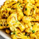 close up on a pile of roasted curried cauliflower on a white plate.