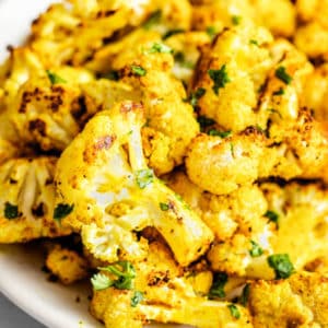 close up on a pile of roasted curried cauliflower on a white plate.