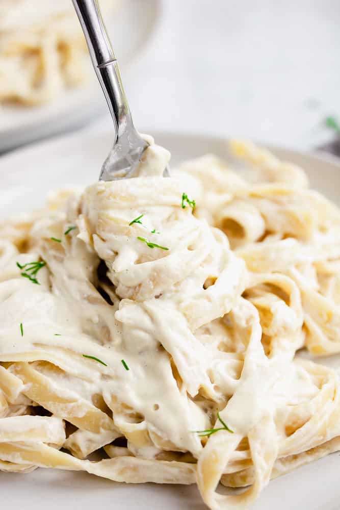 fork holding creamy vegan alfredo sauce on fettuccine