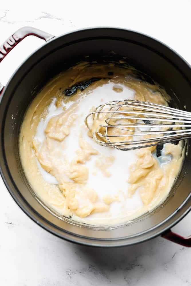 a pot with thick mixture and milk added with a whisk