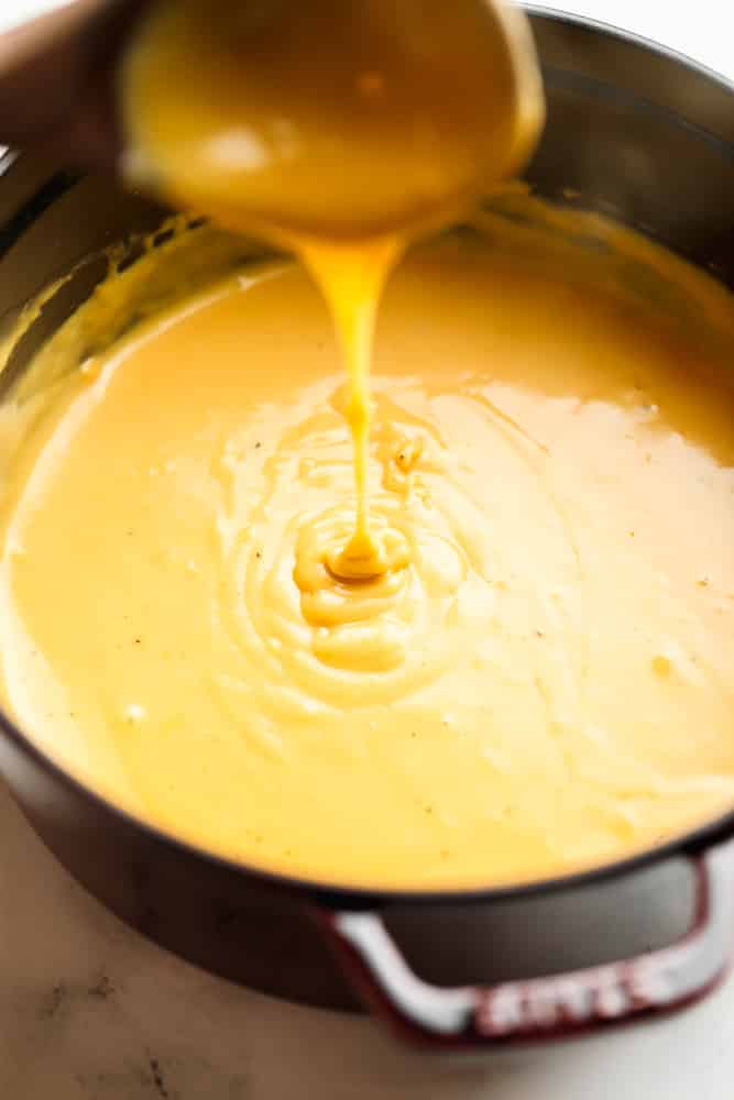 pan full of beer cheese dip, a spoon is drizzling some into the pot
