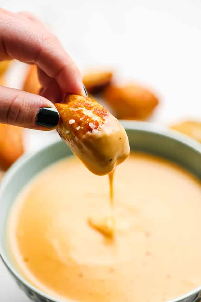 pretzel bite being dipped into cheese sauce, pulled out showing it dripping down into the bowl