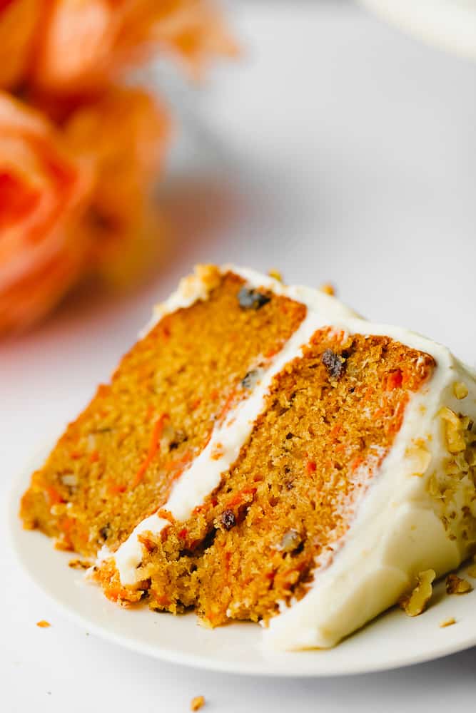piece of vegan carrot cake on a plate with orange flower in background