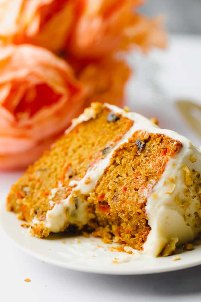 a bite taken from a big slice of vegan carrot cake with orange flowers in background
