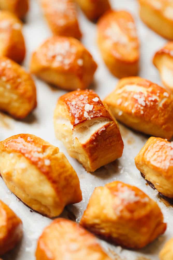 lots of pretzel pieces on a parchment lined baking sheet with salt, golden brown