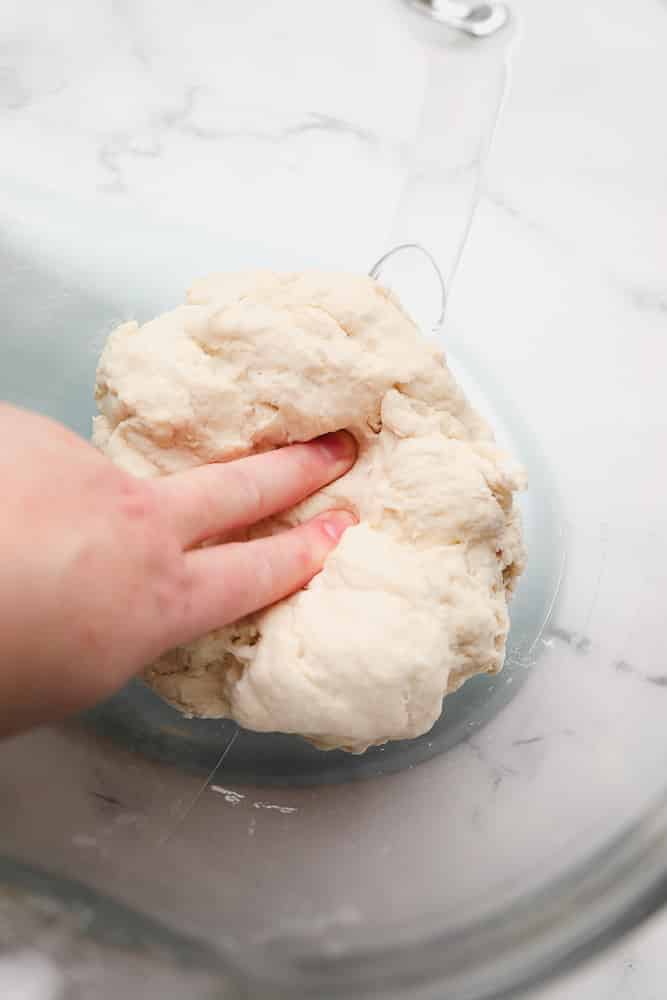 fingers pushing into dough in a glass bowl