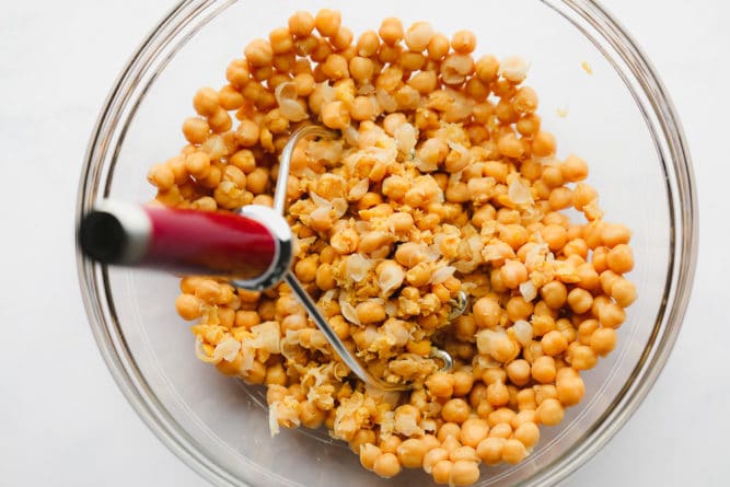 bowl of chickpeas being mashed with a potato masher