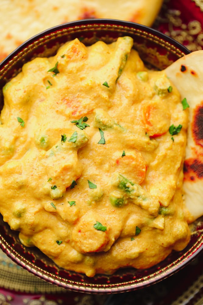 korma curry in a reddish bowl with cilantro and naan