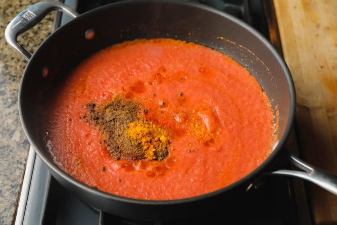 spices being added to pan with red sauce