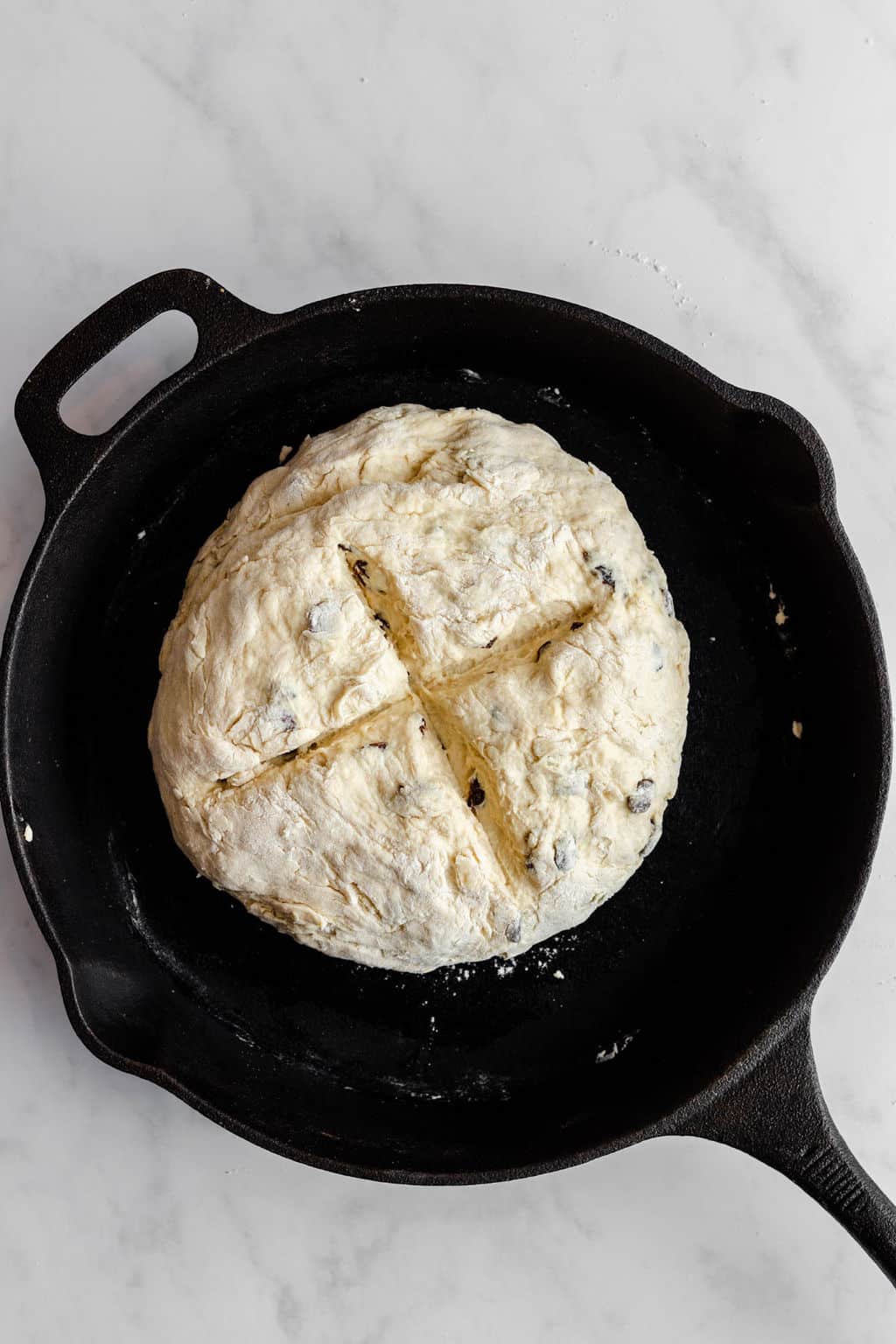 a scored ball of vegan Irish soda bread dough in a black cast iron pan.