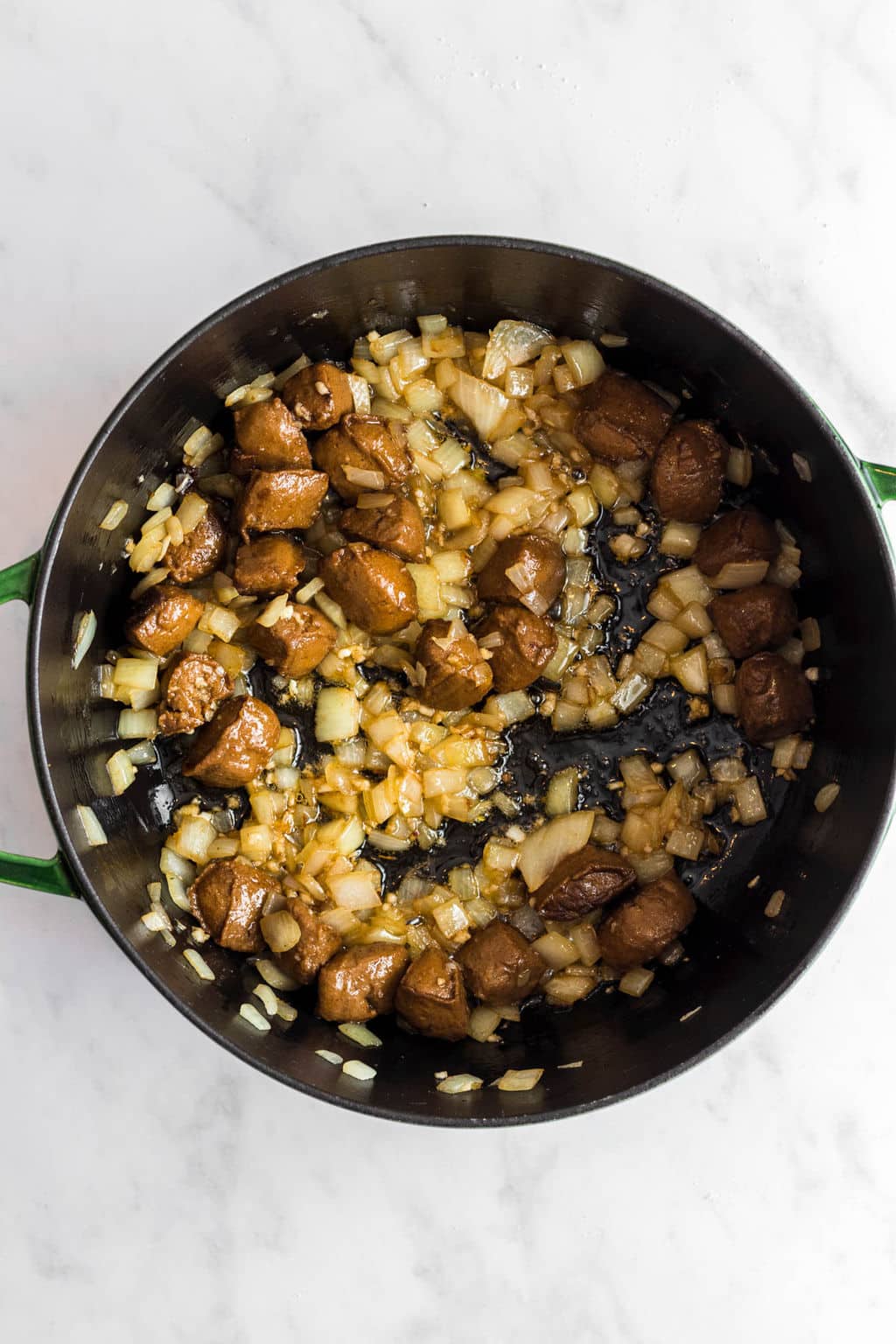 cooking vegan sausage and onions in a large black skillet.