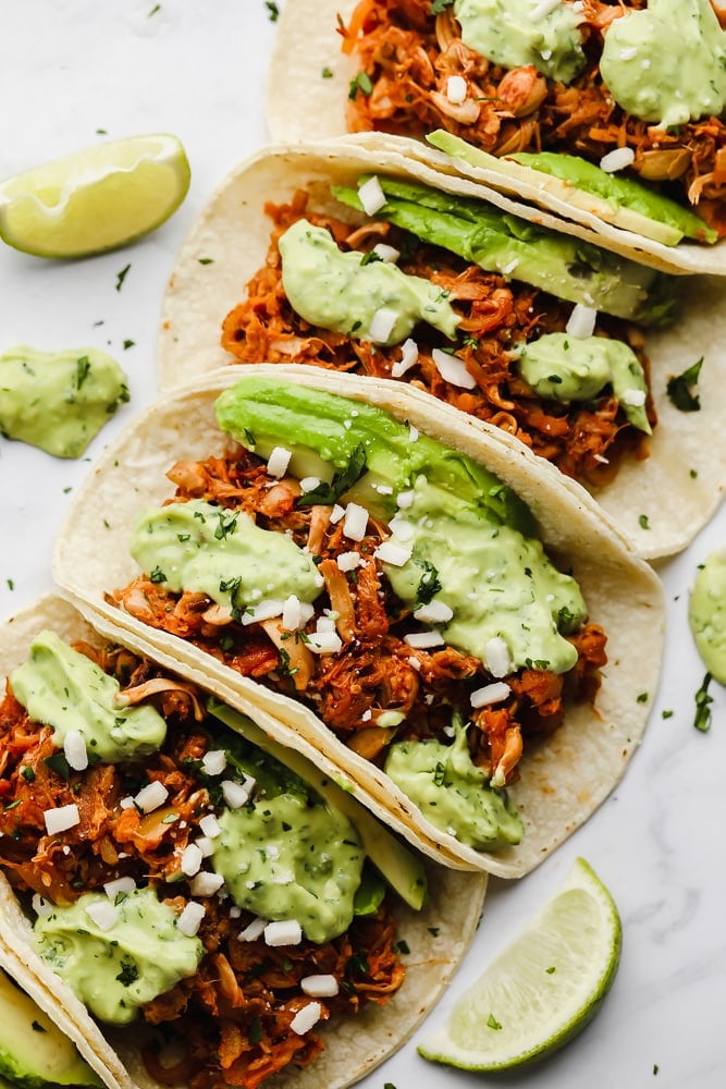 jackfruit tacos topped with a green avocado sauce lined up in a row.
