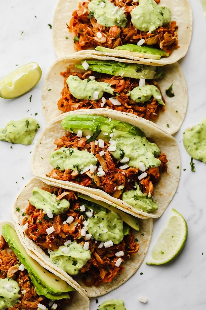 jackfruit tacos topped with a green avocado sauce lined up in a row.