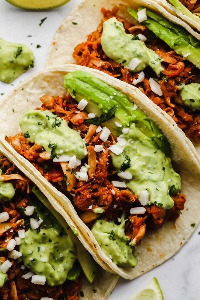 close up on jackfruit tacos topped with a green avocado sauce.