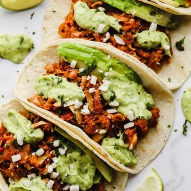 close up on jackfruit tacos topped with a green avocado sauce lined up in a row.