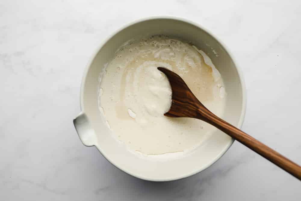 a wooden spoon stirring pancake batter in a white bowl.