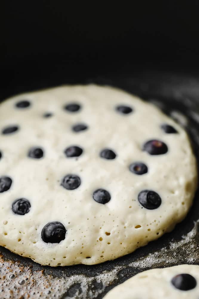 a vegan blueberry pancake cooking on a black griddle.