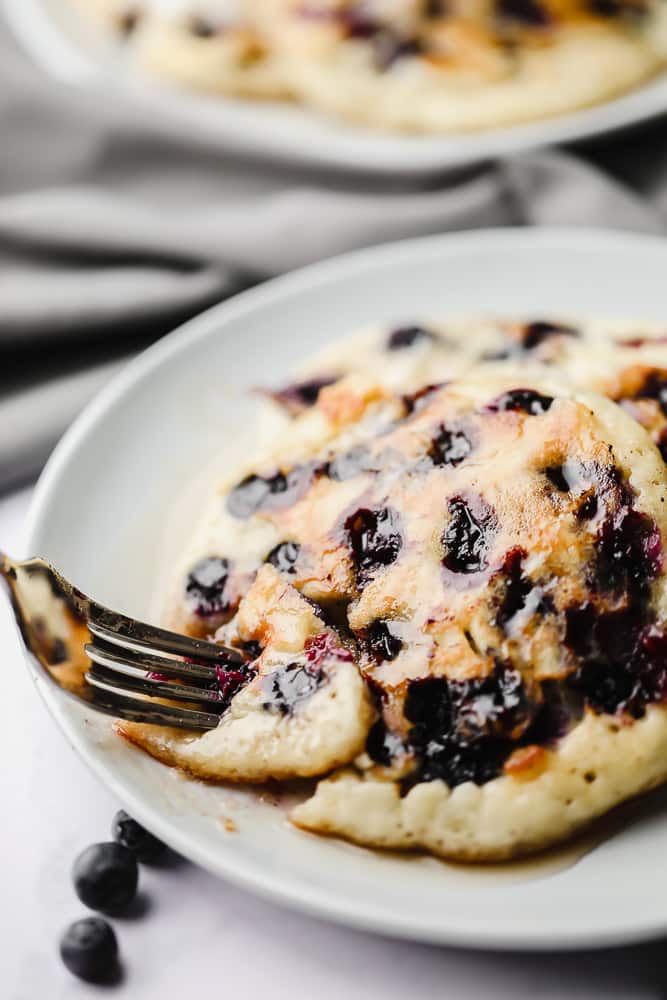 a fork taking a bite out of vegan blueberry pancakes.