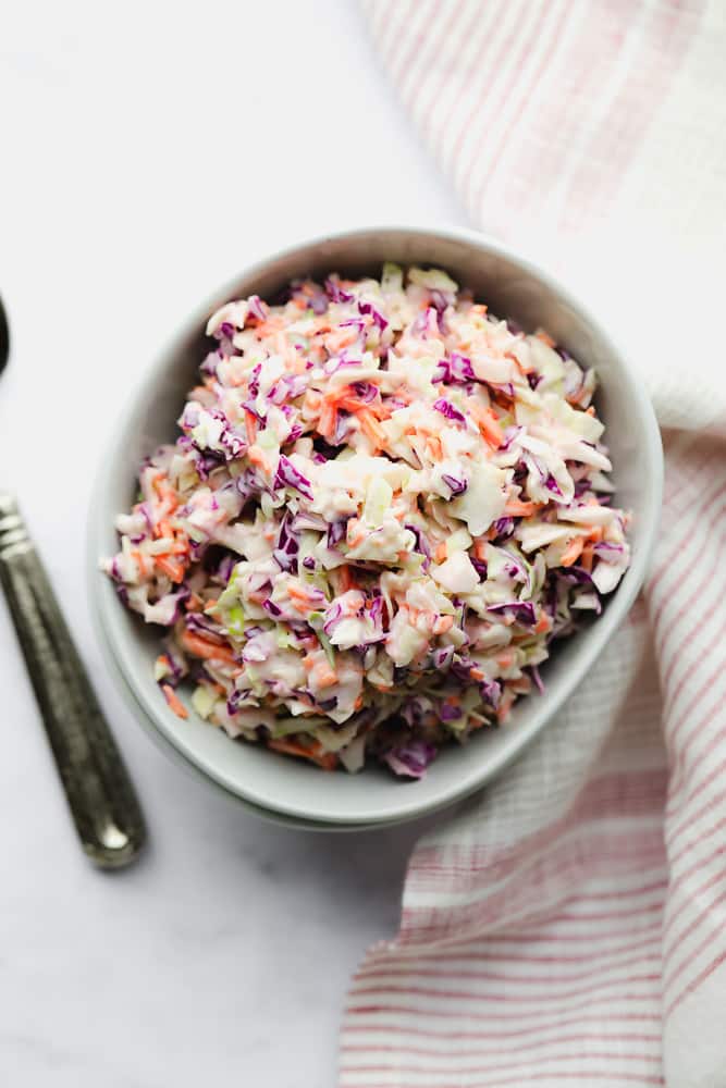 looking down on a bowl of vegan coleslaw in white bowls, red and white striped towel