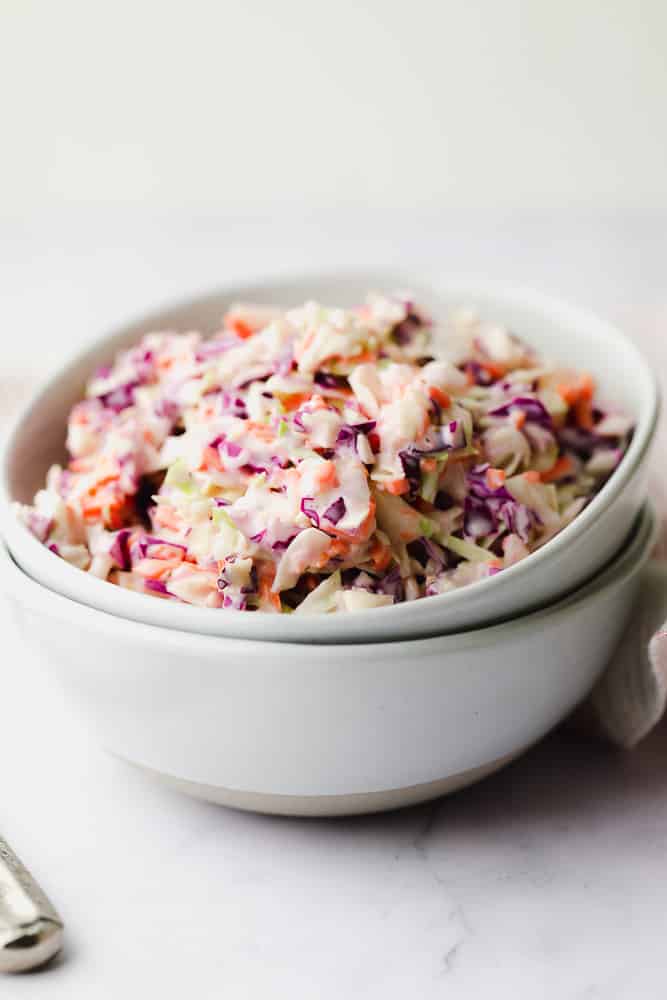 two bowls resting inside each other, top one filled with purple, orange and green cabbage