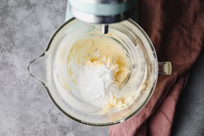 powdered sugar being added to butter in glass bowl