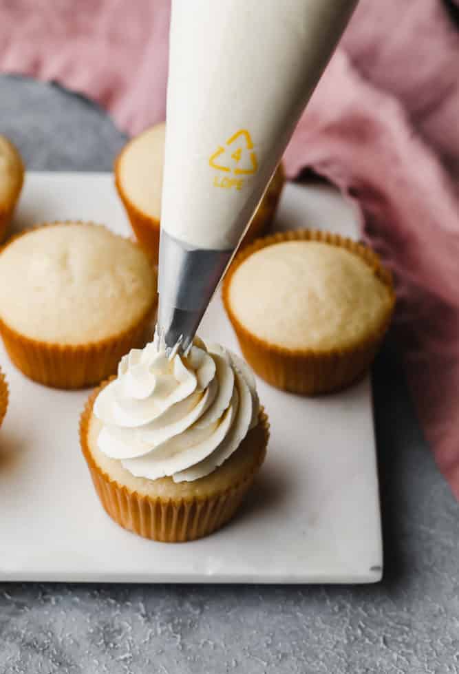 piping bag with frosting, showing finishing frosting a cupcake