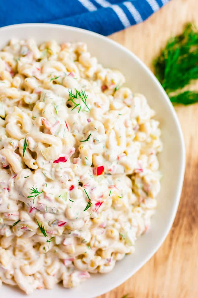 showing half a large bowl filled with macaroni salad on wood backboard