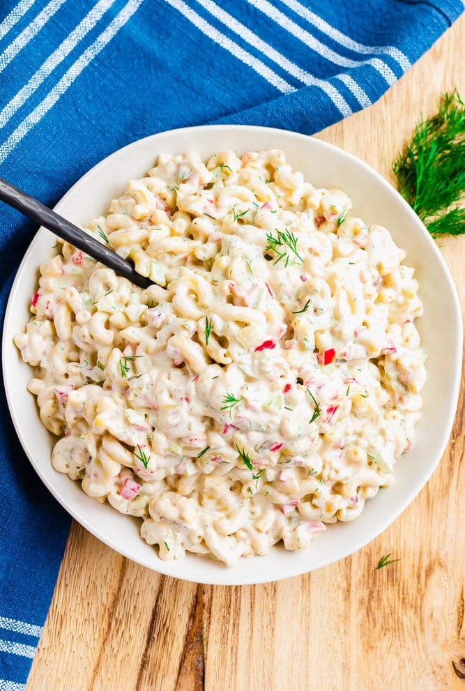large bowl with vegan macaroni salad, a spoon and blue towel in background