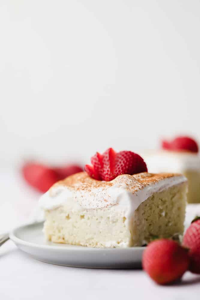 a piece of milk soaked cake with whipped cream and strawberries on a plate