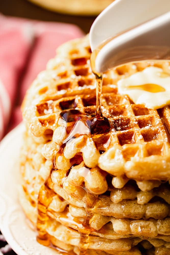 syrup being drizzled on stack of vegan waffles, red towel in background