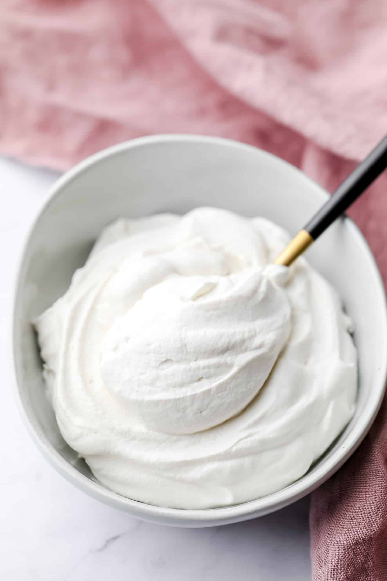 a spoon scooping a dollop of vegan whipped cream out of a white bowl.