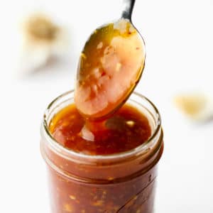 a sauce-covered spoon coming out of a jar of stir fry sauce.