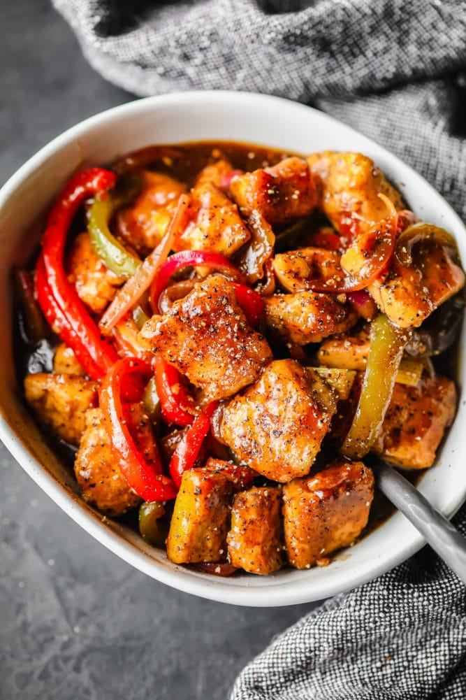 white bowl with black pepper tofu and peppers, grey/black background and towel