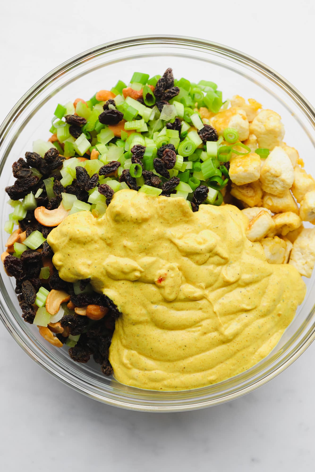 vegetables, baked tofu, and a creamy yellow sauce together in a large glass bowl.